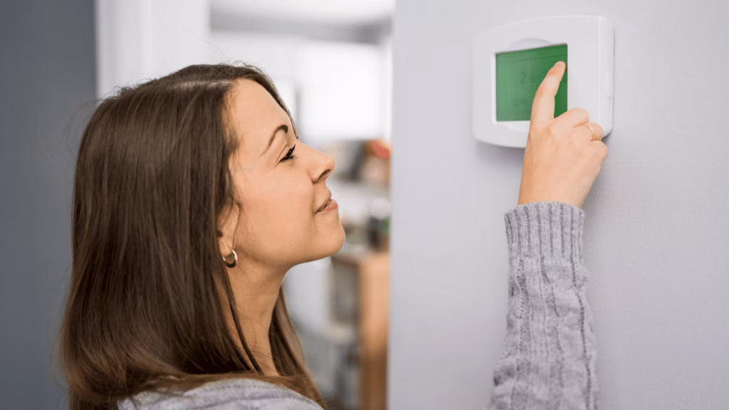 woman adjusting thermostat in home during the winter